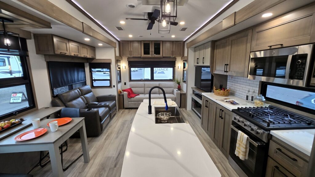 Modern RV interior featuring a spacious kitchen with stainless steel appliances and a cozy living area with a sofa and recliner.